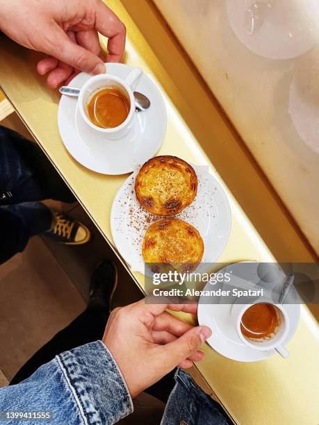 eating pastel de nata pastry with espresso coffee at a bakery in lisbon, personal perspective view - egg tart stockfoto's en -beelden