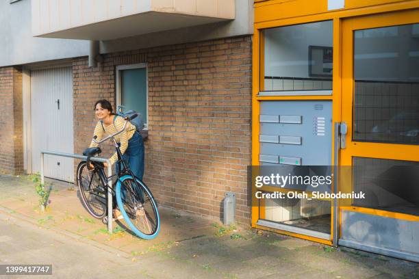 woman locking bicycle in the residential neighbourhood - fastening stockfoto's en -beelden