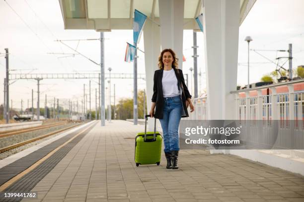woman walking at the railroad station, dragging her suitcase and smiling at camera - sleep walking stockfoto's en -beelden