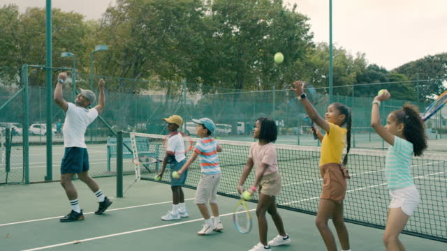 코치와 테니스를하는 어린이 그룹. 행복하고 귀엽고 다양한 테니스 선수들에게 코트에서 라켓을 사용하도록 가르치는 남자