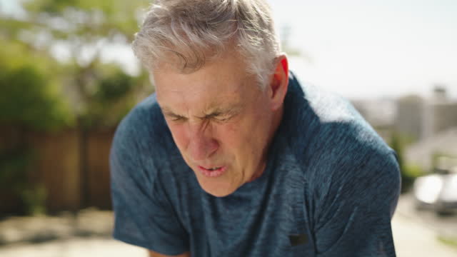 A senior man feeling tired after running outside during exercise. A mature guy, out of breath, looking unhappy and weak during his fitness routine