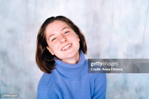 beautiful young woman with short hair and gray eyes laughing against gray wall background. she is wearing a violet sweater. close-up portrait. concept of natural beauty - high collar stock-fotos und bilder