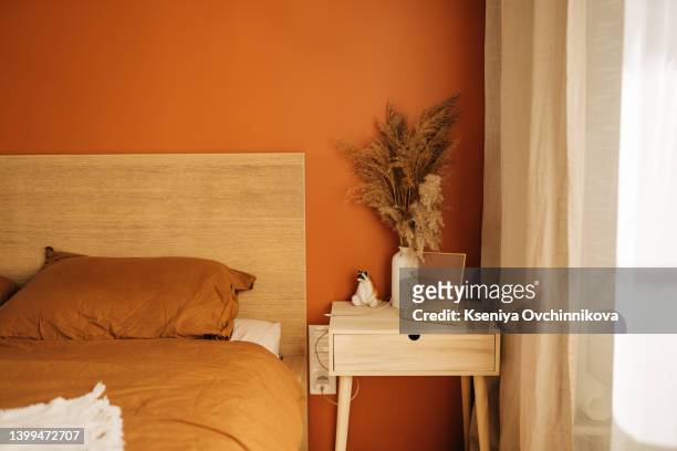 close-up on simple, white bedside table with decorations next to comfortable bed in bedroom with dark blue wall - terrakotta stock-fotos und bilder