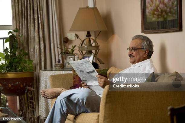 alter mann liest zeitung auf dem sofa zu hause - newspaper luxury stock-fotos und bilder