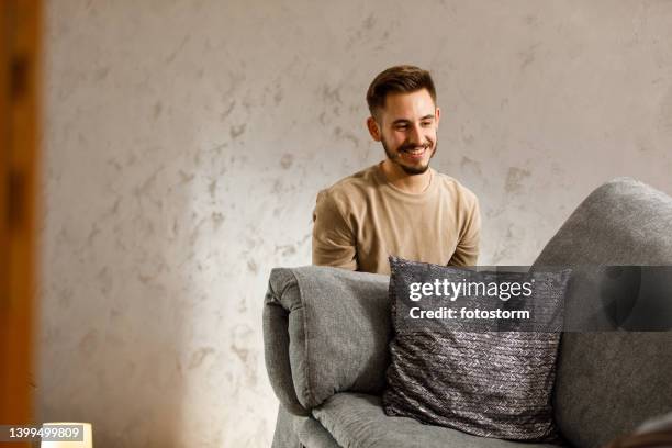 smiling young man lifting the sofa, moving it someplace else in his new living room - carrying sofa stock pictures, royalty-free photos & images