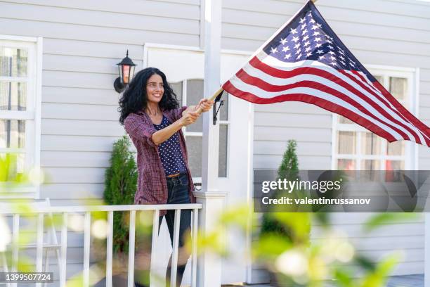 mid adult woman hangs a american flag on her porch and celebrating fourth of july. independence day. - democratic women of the house stock pictures, royalty-free photos & images