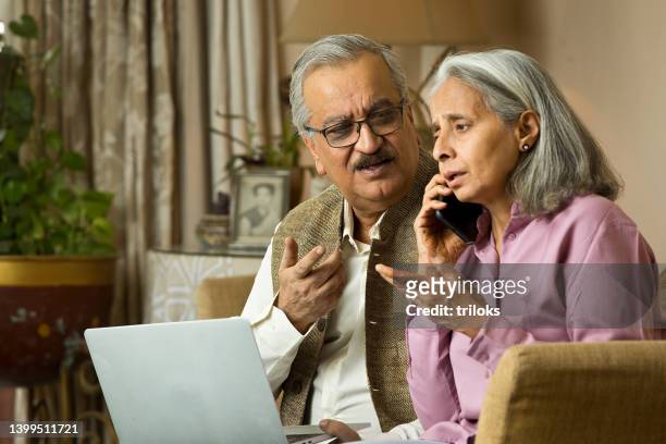 stressed old couple using laptop and talking on mobile phone at home - frustrated on phone stock pictures, royalty-free photos & images