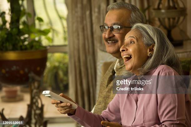 old couple watching tv using remote control - indian elderly couple stock pictures, royalty-free photos & images