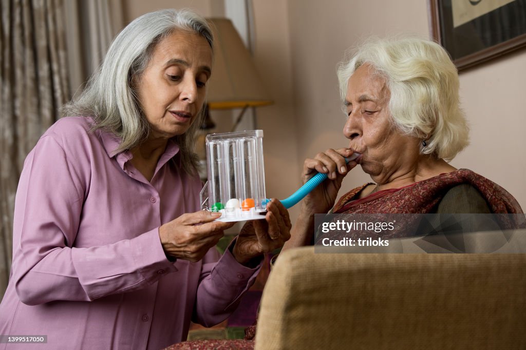 Elderly woman supporting her female friend after using a spirometer to stimulate lung