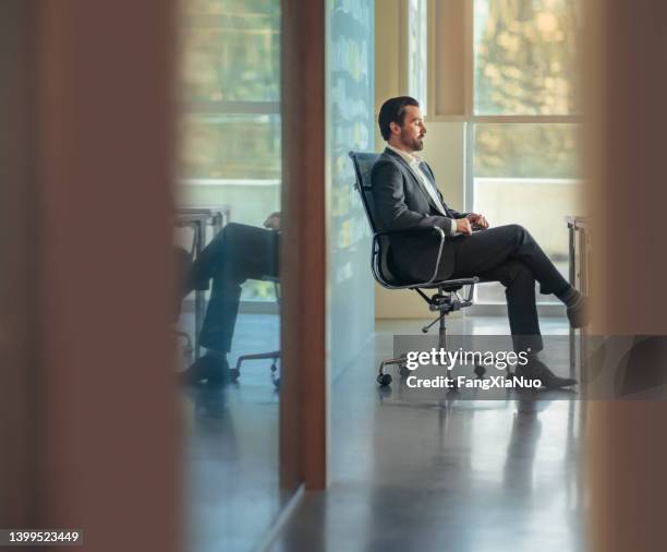 geschäftsmann, der mit geschlossenen augen auf dem stuhl sitzt und meditiert, der sich allein im geschäftsbüro entspannt - mindfulness stock-fotos und bilder