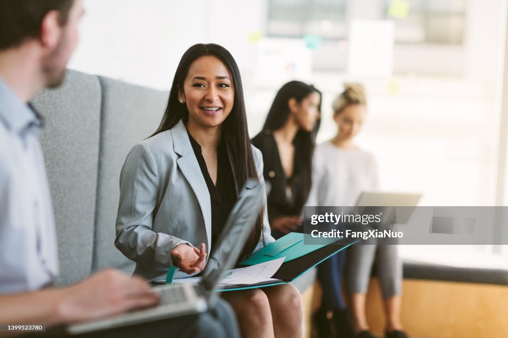 Multiracial young woman sits to discuss with work colleagues plans and ideas in modern coworking shared business office