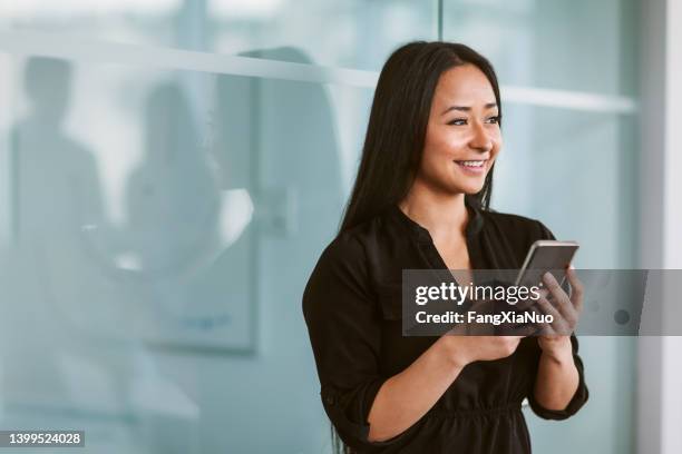 donna cinese ispanica asiatica multirazziale di razza mista che invia messaggi al telefono mentre guarda di lato nel moderno ufficio commerciale - indians foto e immagini stock