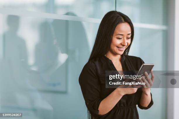 mulher asiática multirracial mestiça enviando mensagens ao telefone no escritório de negócios moderno - etnias asiáticas e indias - fotografias e filmes do acervo