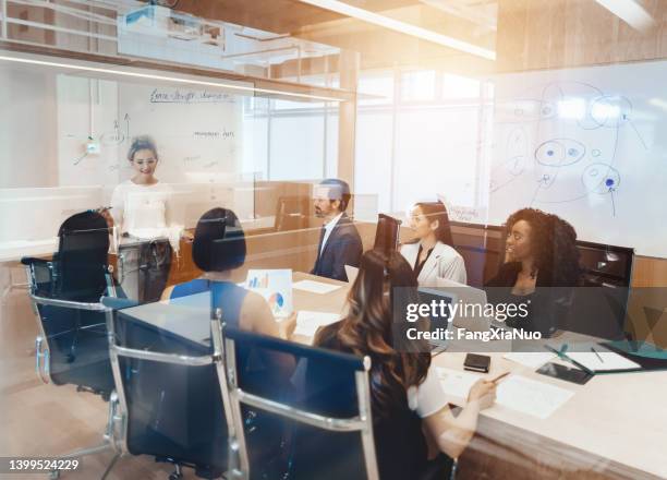 caucasian young woman leads colleagues in a meeting discussion in a conference room in business office with diverse multicultural colleagues - masters degree imagens e fotografias de stock