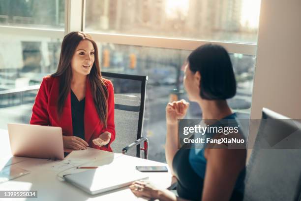 two business women colleagues discussing project together in modern office - red backgrounds stock pictures, royalty-free photos & images