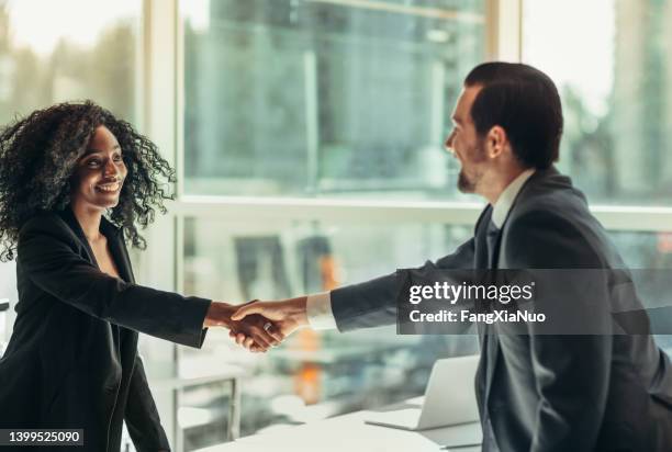 black businesswoman shakes hand with businessman across table desk in modern business office well-dressed after agreement partnership job interview - initiative stock pictures, royalty-free photos & images