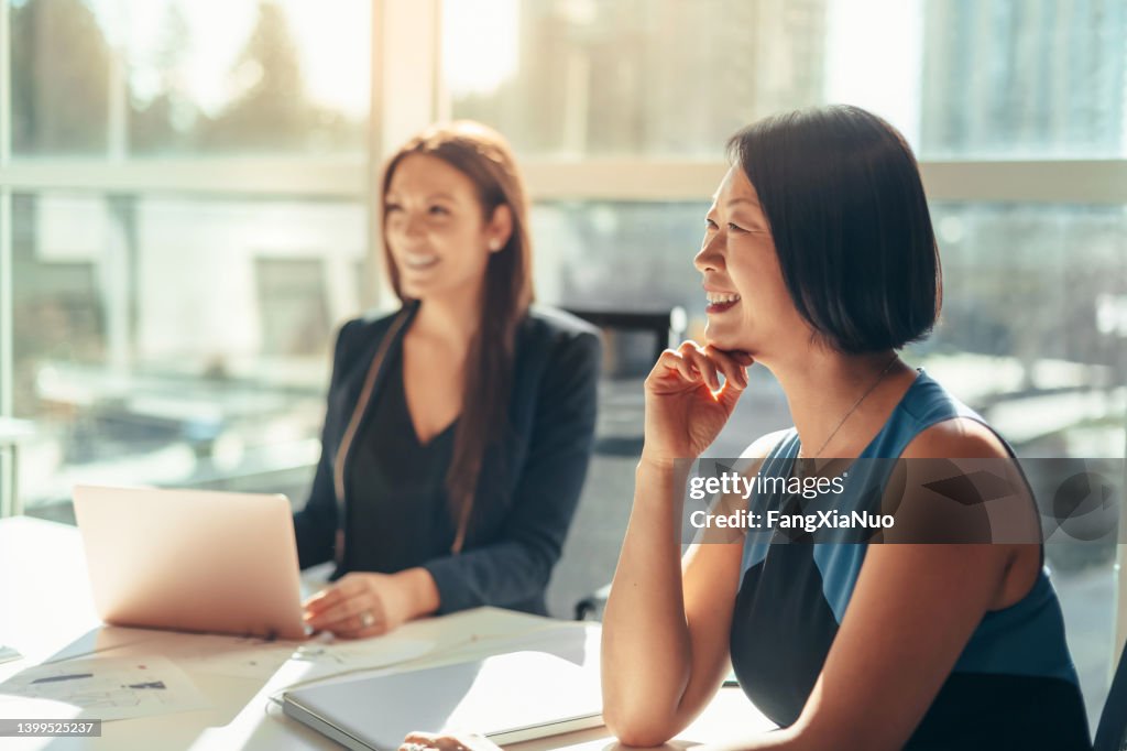 Korean businesswoman listening to discussion at meeting with colleague in modern business office