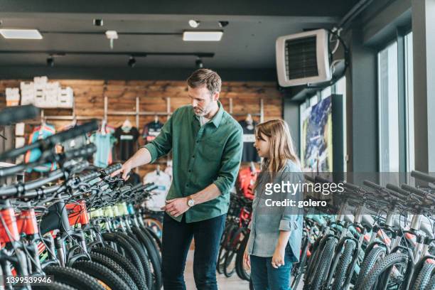 homme montrant un nouveau vélo à une petite fille dans un magasin de vélos - magasin de sport photos et images de collection