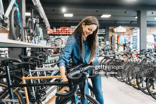 glückliche frau, die sich ein neues fahrrad im bikeshop ansieht - buying a bike stock-fotos und bilder