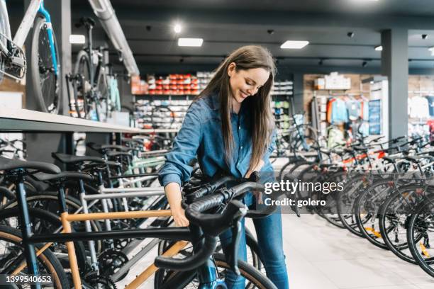 happy woman looking at new bicycle in bikeshop - buying a bike bildbanksfoton och bilder