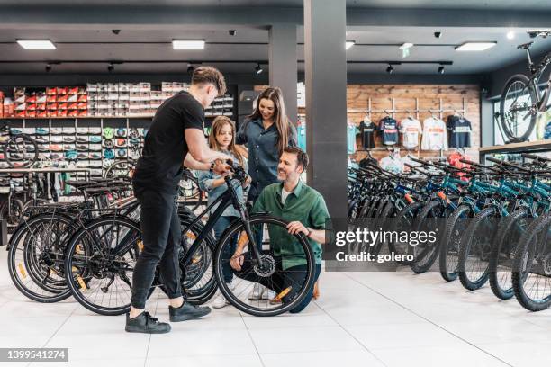 mann zeigt junger familie im bikeshop neues fahrrad - buying a bike stock-fotos und bilder