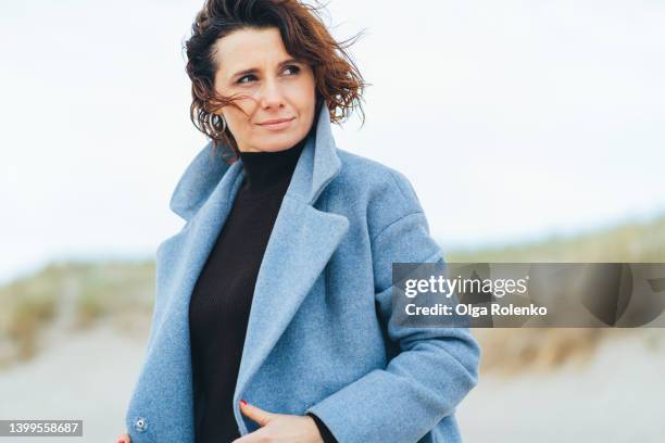 fashionable woman standing and thinking on the cold beach - mature female models stock pictures, royalty-free photos & images