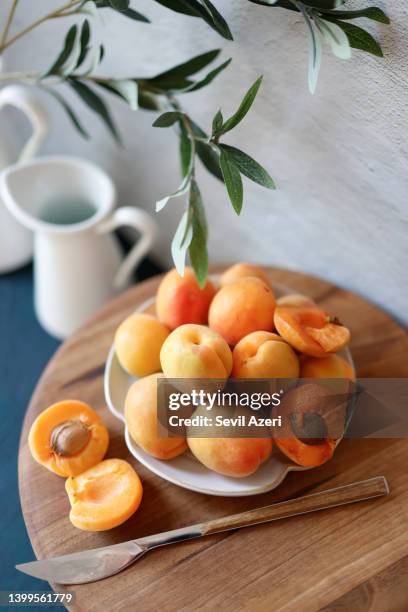 albaricoques maduros en una placa de cerámica blanca sobre una tabla de presentación de madera de nogal - apricot fotografías e imágenes de stock