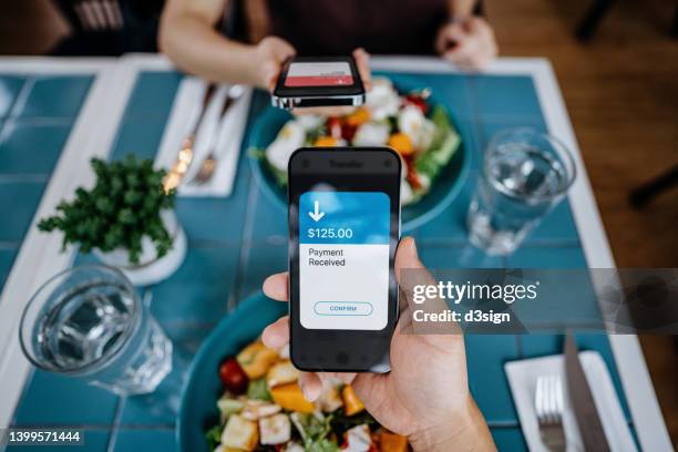 personal perspective of man holding smartphone, splitting bills with friend while dining in restaurant. sending / receiving payment of the meal through digital wallet device on smartphone. smart banking with technology - straight stockfoto's en -beelden