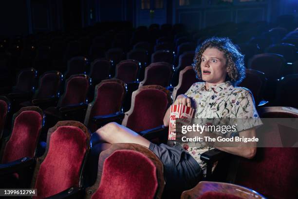 young man watching scary movie alone in theater - horror movie stock-fotos und bilder