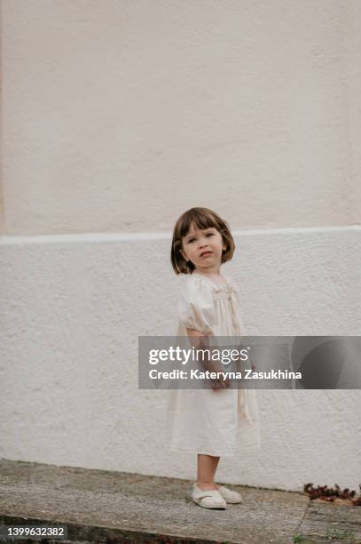 a vertical portrait of a toddler girl in a white linen summer dress on a white background - mini short stockfoto's en -beelden