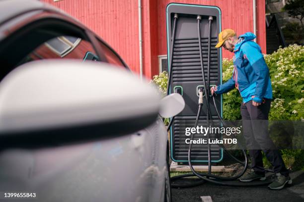 a male driver pours fuel into a car at a gas station during the day. - tesla model s stock pictures, royalty-free photos & images
