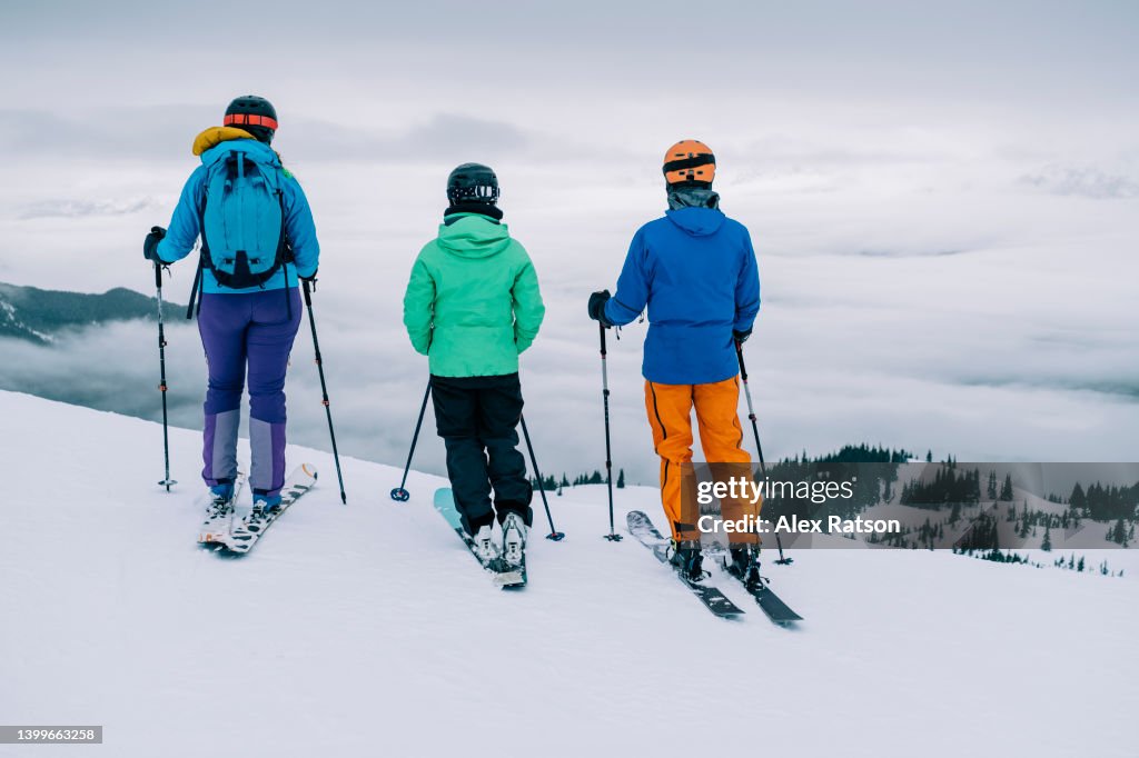 Three friends stand together looking at a mountain view while skiing