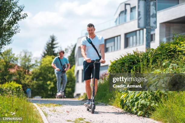 mature multi-ethnic male friends and work colleagues riding motor scooters in a public park - electric push scooter stock pictures, royalty-free photos & images