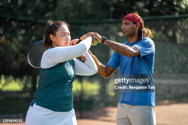 femme asiatique chinoise de milieu adulte apprenant le tennis de son entraîneur sur un court de tennis pendant la matinée du week-end - tennis coaching photos et images de collection