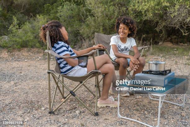 young boy and girl talking while sitting outdoors at the campsite while camping in the nature. - frat boys stock pictures, royalty-free photos & images