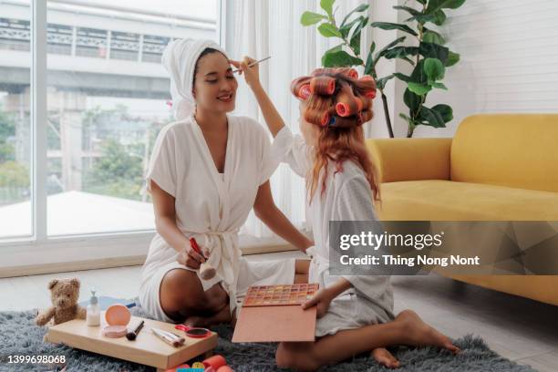 little girl doing makeup to mom. mother and daughter have fun together. - asian mom kid kiss stock-fotos und bilder