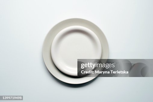 A white-gray plate lies on a white background. Minimalism. Empty plate for food. Culinary background. A white-gray plate lies on a white background. Minimalism. Empty plate for food. Culinary background.