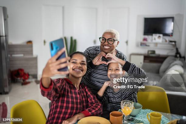 young woman doing a video call (or taking a selfie) with her family on breakfast time at home - misses vlog stock pictures, royalty-free photos & images