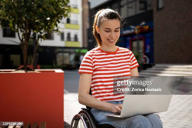woman in wheelchair in front of a building using laptop - multiple sclerose stockfoto's en -beelden