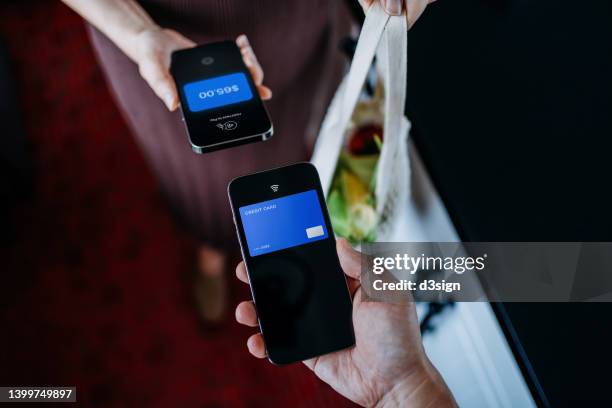 hands of customer and shop owner holding smartphone, sending / receiving payment of grocery shopping through digital wallet on smartphone in store. carrying a bag of fresh groceries in reusable cotton mesh bag. contactless pay. point of sale - economía colaborativa fotografías e imágenes de stock