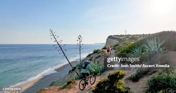 mountain biking couple follow trail along cliff - algarve stock-fotos und bilder