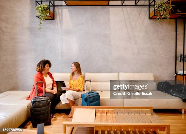 smiling businesswomen with luggage using a tablet on a hotel lobby sofa - diversity showcase arrivals stock pictures, royalty-free photos & images