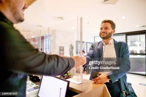 joven y sonriente hombre de negocios que se registra en un hotel durante un viaje de negocios - welcoming guests fotografías e imágenes de stock