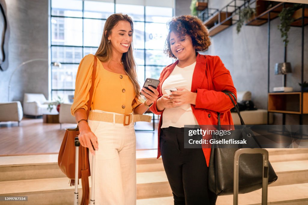Two smiling businesswomen using smart phones to share files in a hotel lobby