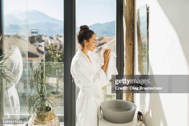 smiling woman cleaning her hands with white towel. personal hygiene and morning routine - woman in bathroom stockfoto's en -beelden
