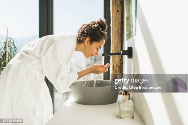 young woman awakening, washing and cleaning her face with splashing water - beautification fotografías e imágenes de stock