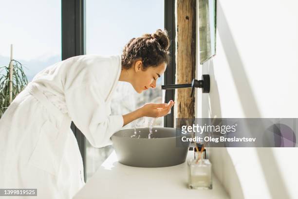 young woman awakening, washing and cleaning her face with splashing water - beauty care stock pictures, royalty-free photos & images