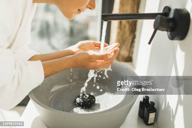 young woman awakening, washing and cleaning her face with splashing water. unrecognisable person - beauty treatment fotografías e imágenes de stock