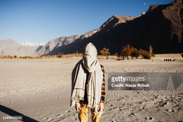 der mann, der in der kalten katpana-wüste zwischen den karakorum-bergen bei sonnenuntergang traditionellen schal trägt - pashtun stock-fotos und bilder