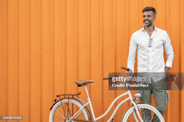 man posing with his bicycle against orange background - fotografia de três quartos imagens e fotografias de stock
